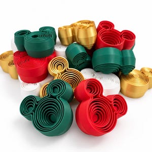 May include: A collection of three-dimensional Mickey Mouse head-shaped objects in red, dark green, gold, and white. Each piece features a layered, concentric circular design with a hollow center, arranged in a cluster on a white surface.