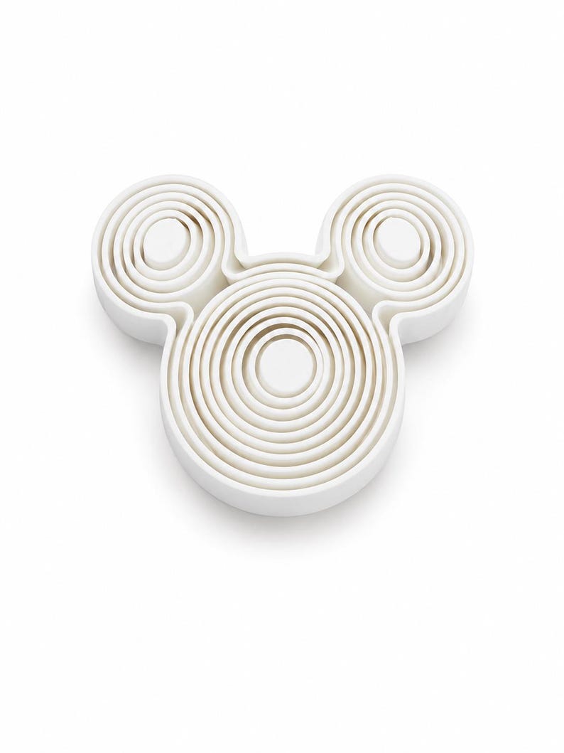 Puede incluir: Un juego de cortadores de galletas de pl&aacute;stico blanco con forma de cabeza de rat&oacute;n, que presenta un marco circular central grande y dos orejas circulares m&aacute;s peque&ntilde;as, con m&uacute;ltiples anillos conc&eacute;ntricos anidados que crean un efecto escalonado.
