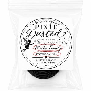 Puede incluir: Una bolsa de pl&aacute;stico transparente resellable que contiene un objeto circular negro. Una etiqueta circular blanca presenta la silueta de un hada negra, estrellas y el texto: YOU'VE BEEN PIXIE Dusted BY THE Meeks Family STATEROOM 7106 A LITTLE MAGIC JUST FOR YOU.