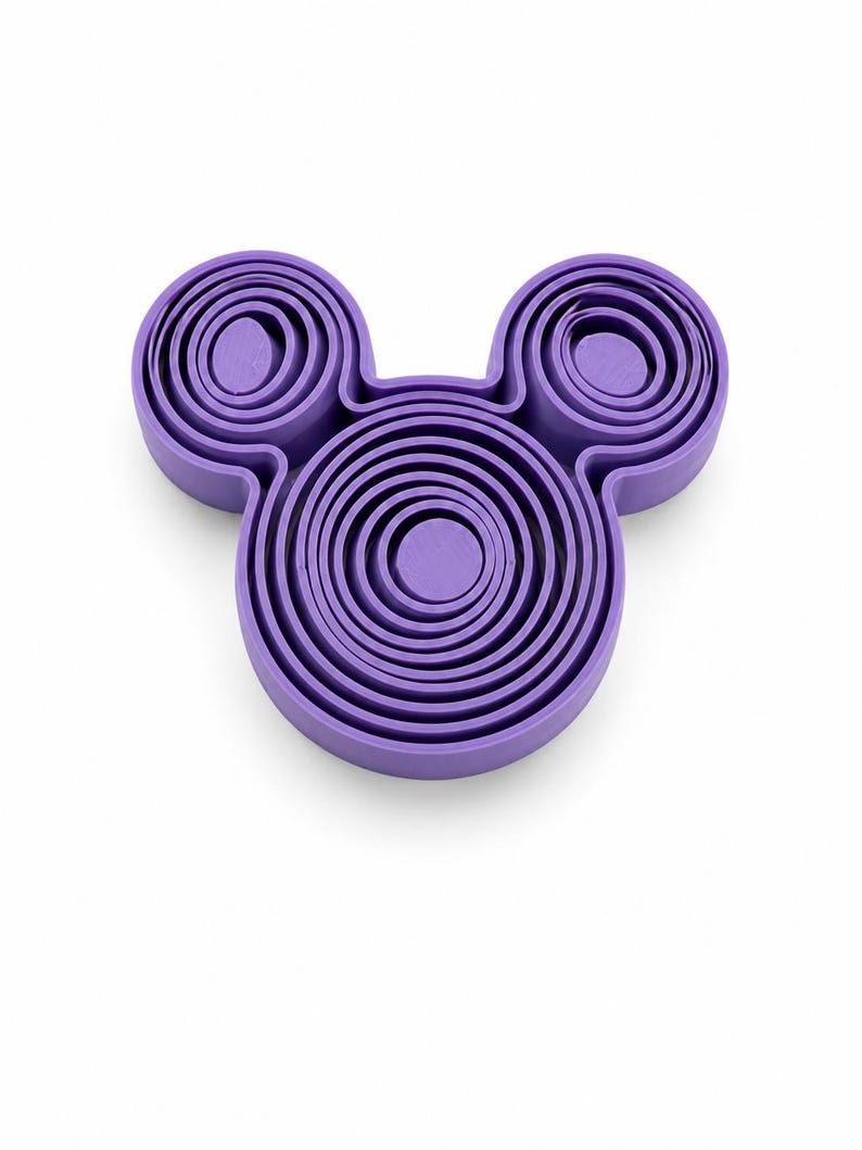 Puede incluir: Un juego de cortadores de galletas de pl&aacute;stico morado con forma de silueta de cabeza de rat&oacute;n. El dise&ntilde;o presenta un marco circular central grande con dos marcos circulares m&aacute;s peque&ntilde;os en la parte superior, cada uno con varios cortadores de anillos conc&eacute;ntricos.