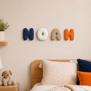 May include: Four individual wall-mounted letters spelling the name NOAH. The letter N is dark blue, the O is white, the A is beige, and the H is orange. Each letter has a rounded, soft, three-dimensional shape with a smooth, matte finish.