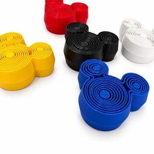 Puede incluir: Una colecci&oacute;n de cinco objetos circulares con forma de cabeza de rat&oacute;n, cada uno con una serie de anillos conc&eacute;ntricos en la superficie superior. Los objetos son de color rojo, amarillo, negro, blanco y azul, dispuestos de forma dispersa.