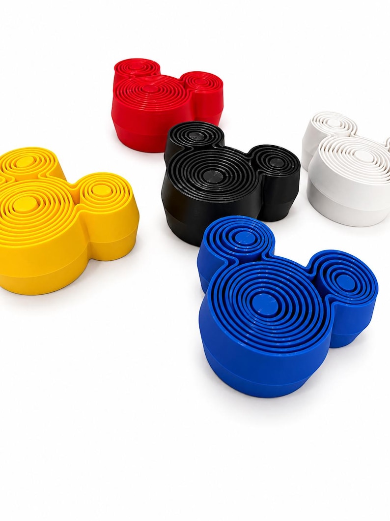 Puede incluir: Una colecci&oacute;n de cinco objetos circulares con forma de cabeza de rat&oacute;n, cada uno con una serie de anillos conc&eacute;ntricos en la superficie superior. Los objetos son de color rojo, amarillo, negro, blanco y azul, dispuestos de forma dispersa.