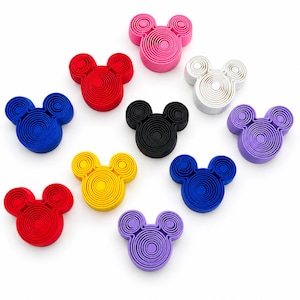 Puede incluir: Una colecci&oacute;n de once cepillos de limpieza facial de silicona con forma de cabeza de rat&oacute;n en varios colores, incluyendo rosa, rojo, blanco, negro, morado, amarillo y azul. Cada cepillo presenta una serie de surcos circulares conc&eacute;ntricos.