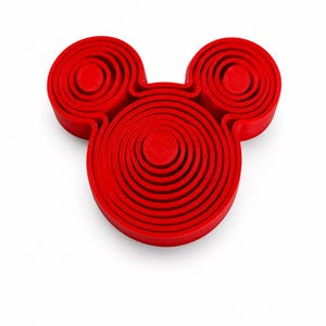 Puede incluir: Un objeto de color rojo brillante con base circular que presenta un anillo central grande y dos anillos m&aacute;s peque&ntilde;os colocados encima, creando una silueta que recuerda a una cabeza con dos orejas. La superficie tiene m&uacute;ltiples crestas circulares conc&eacute;ntricas.