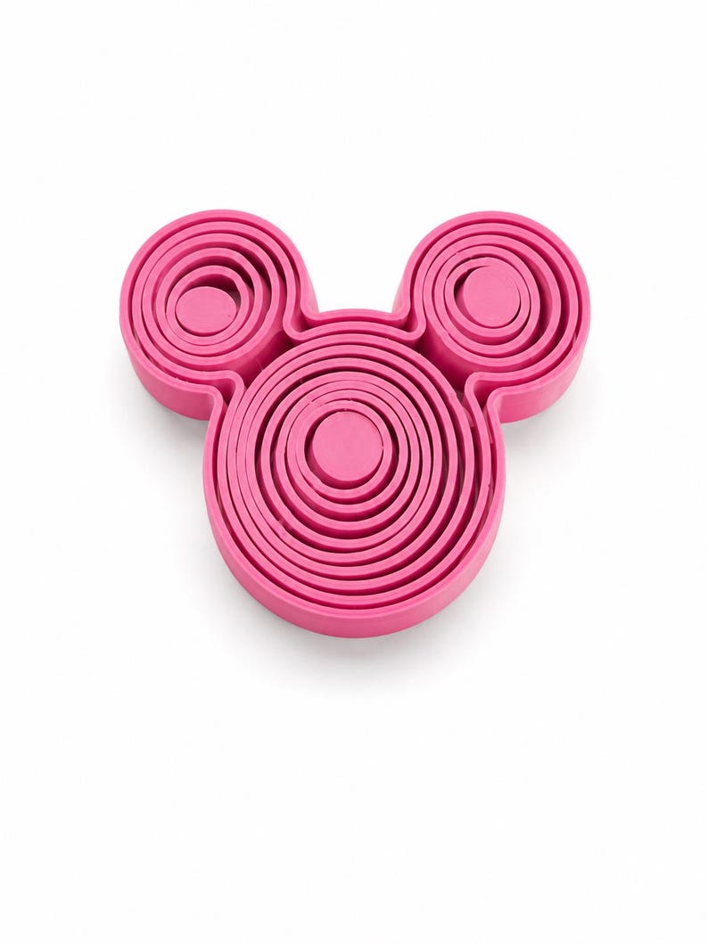 Puede incluir: Un juego de cortadores de galletas de color rosa brillante con forma de cabeza de rat&oacute;n, que presenta un marco circular central grande con dos marcos circulares m&aacute;s peque&ntilde;os unidos en la parte superior, hechos de anillos conc&eacute;ntricos.