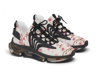 May include: Pair of white sneakers with a floral cherry blossom pattern in pink. The shoes have black accents, laces, and a clear sole. The sneakers are designed for athletic activities and casual wear.