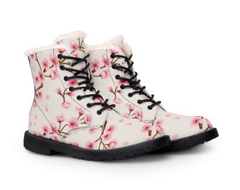 May include: Ankle-high lace-up boots featuring a cream-colored base with a repeating pattern of pink cherry blossoms and brown branches. The boots have black laces, black soles, and a white faux fur lining visible at the top collar.