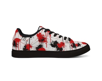 Puede incluir: Zapatillas blancas con suela y cordones negros. Los zapatos presentan un patrón de salpicaduras de pintura roja y negra sobre la superficie blanca. El diseño se repite en los laterales y la parte superior del zapato.