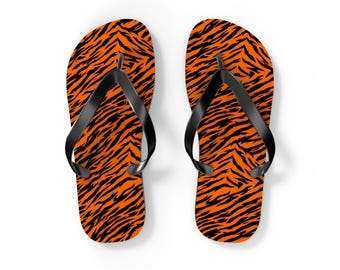 Op de afbeelding: Een paar slippers met een levendig oranje en zwart tijgerstrepenpatroon op de voetbedden. Elke sandaal is voorzien van een effen zwarte rubberen teenslipperband die de voet op zijn plaats houdt voor een consistente uitstraling.