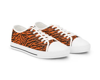 May include: A pair of low-top sneakers featuring a vibrant orange and black tiger stripe pattern across the canvas upper. The shoes include white laces, white rubber toe caps, and white rubber soles with a thin black stripe along the midsole edge.