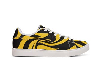 May include: A low-top sneaker featuring a bold black and yellow swirling pattern across the upper. The shoe includes white laces, a white interior lining, and a solid white rubber sole. The design covers the side panels, toe, and heel area.