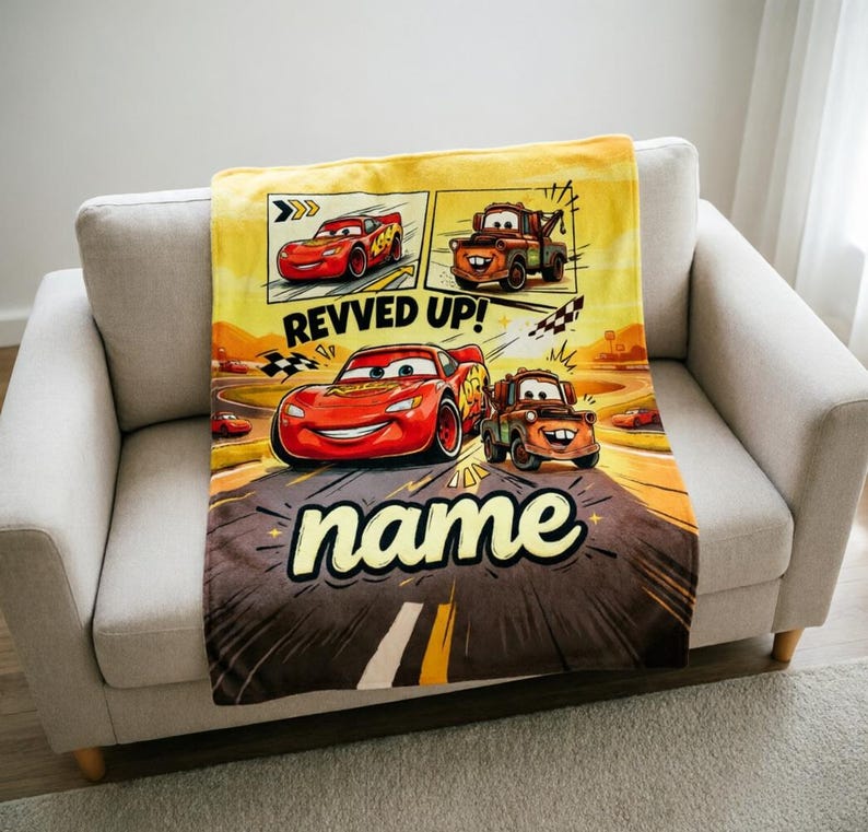 May include: A yellow, brown, and red Cars-themed blanket featuring Lightning McQueen and Mater. The blanket has a comic book style design with the words "Revved Up!" and "name" in a bold font.