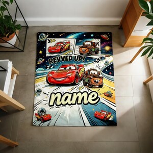 May include: A rectangular, Cars-themed blanket featuring Lightning McQueen and Mater racing on a track. The blanket has a space-themed background with the words "REVVED UP!" and "name" in a playful font. The blanket is designed for children.