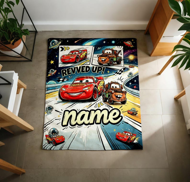 May include: A rectangular, Cars-themed blanket featuring Lightning McQueen and Mater racing on a track. The blanket has a space-themed background with the words "REVVED UP!" and "name" in a playful font. The blanket is designed for children.