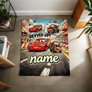 May include: A rectangular blanket featuring Lightning McQueen and Mater from the Cars movie. The blanket has a comic strip design with the words "REVVED UP!" and "name" in a stylized font. The blanket is primarily gray, red, and blue.