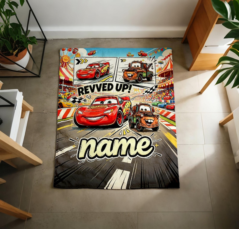 May include: A rectangular blanket featuring Lightning McQueen and Mater from the Cars movie. The blanket has a comic strip design with the words "REVVED UP!" and "name" in a stylized font. The blanket is primarily gray, red, and blue.