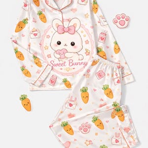 Pu&ograve; includere: Set pigiama in raso bianco con un motivo ripetuto di carote, cuori e buste. La parte superiore presenta una grafica di coniglietto dei cartoni animati con il testo "Sweet Bunny". Il set include una camicia abbottonata a maniche lunghe e pantaloni abbinati.