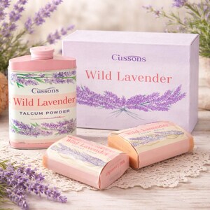 May include: A collection of Cussons Wild Lavender products, including talcum powder, soap, and a box. The products feature a lavender design and the text "Wild Lavender". The items are arranged on a white lace doily with lavender sprigs.