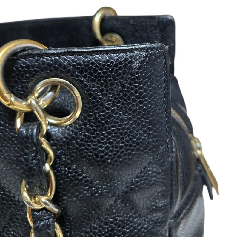 May include: Close-up of a black leather handbag with gold-tone hardware. The bag features a quilted pattern and a chain strap. The zipper pull and rings are gold. The leather has a pebbled texture.
