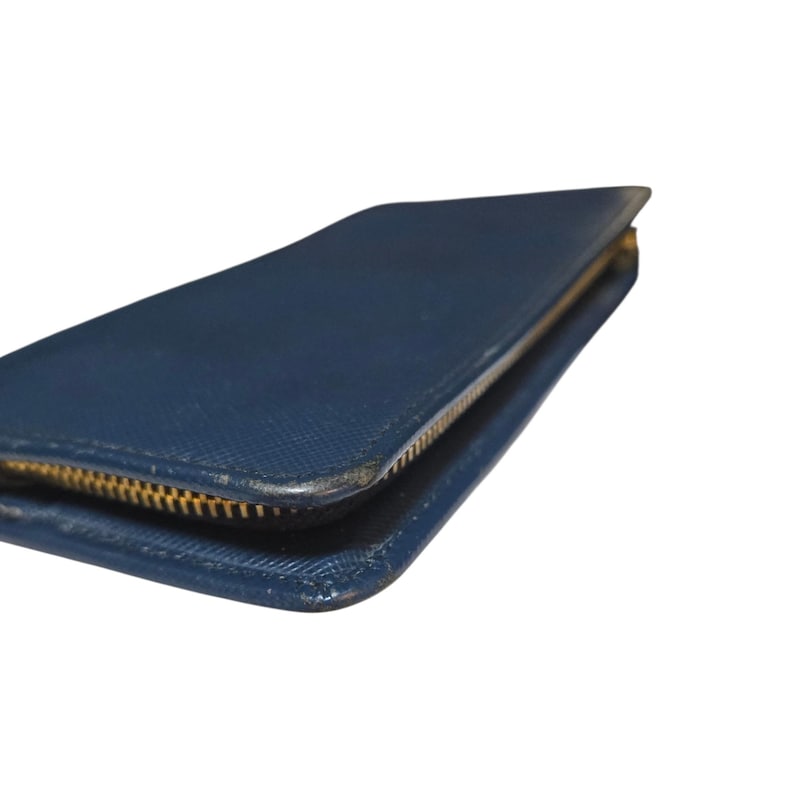 May include: A blue wallet with a gold zipper. The wallet is rectangular and appears to be made of leather. The zipper runs along three sides of the wallet. The wallet is closed.