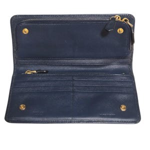 May include: Open navy blue leather wallet with multiple compartments, including a zippered section and card slots. The wallet features gold-toned hardware, including zippers and snap closures. The interior is also navy blue.