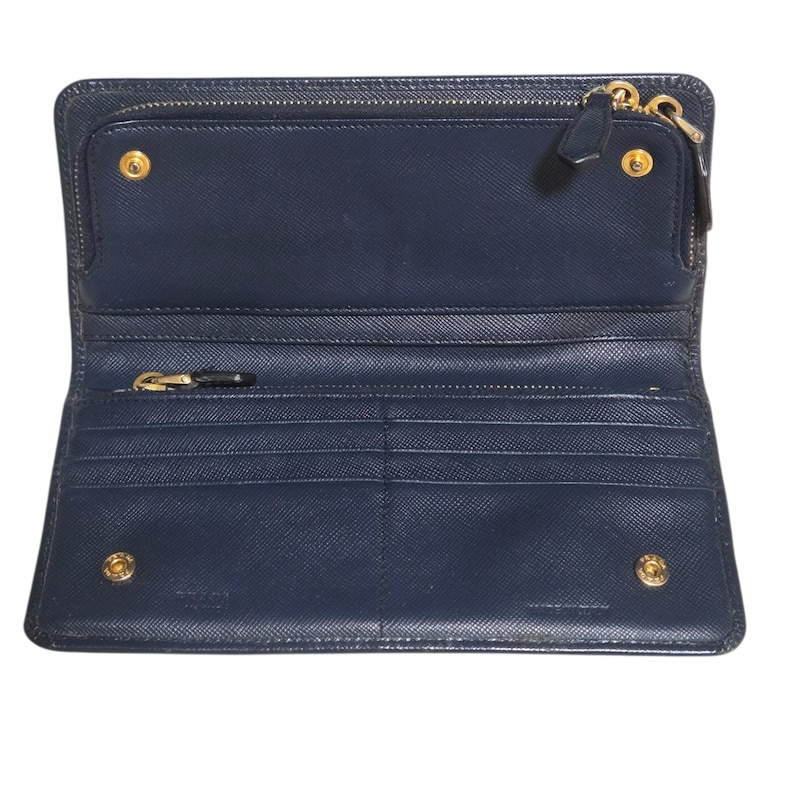 May include: Open navy blue leather wallet with multiple compartments, including a zippered section and card slots. The wallet features gold-toned hardware, including zippers and snap closures. The interior is also navy blue.