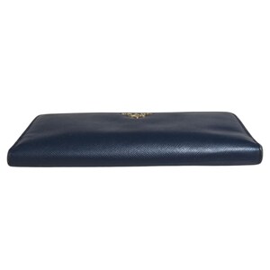 May include: A navy blue leather wallet with a gold-colored logo. The wallet is rectangular and appears to be closed. The leather has a textured appearance. The wallet is a luxury item.