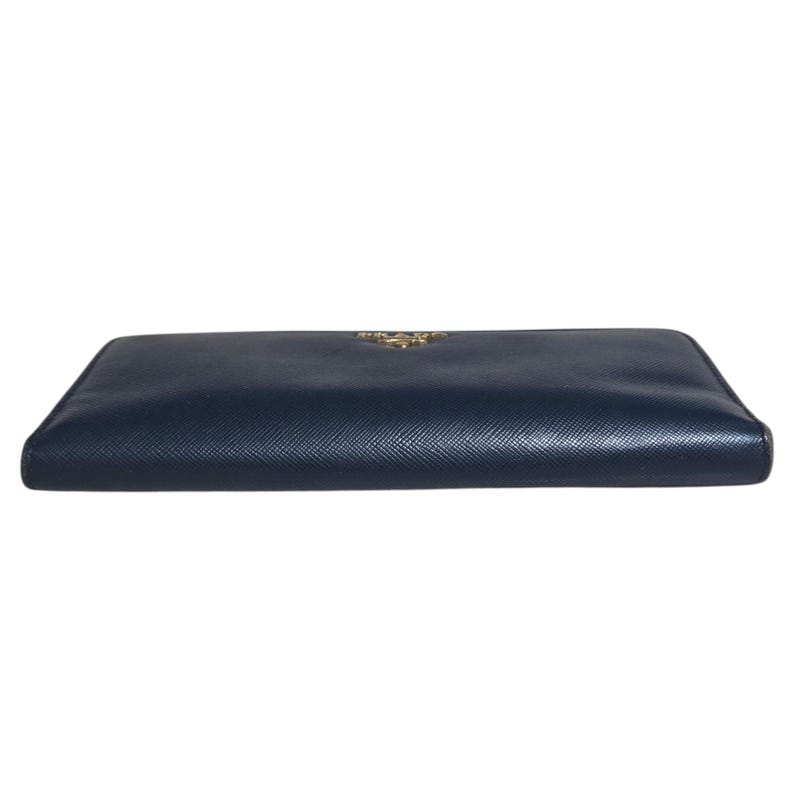 May include: A navy blue leather wallet with a gold-colored logo. The wallet is rectangular and appears to be closed. The leather has a textured appearance. The wallet is a luxury item.