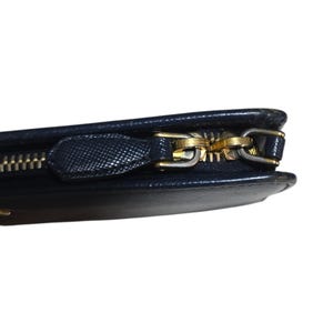 May include: Close-up of a navy blue wallet with a gold-colored zipper. The wallet has a textured surface and a gold zipper pull. The zipper is partially open, revealing the interior.