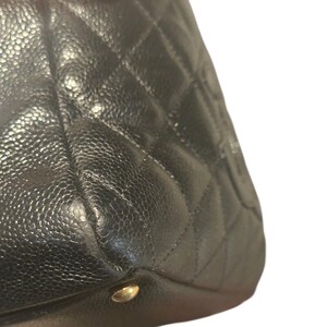 May include: Close-up of a black leather handbag with a diamond-quilted pattern. The bag has a textured surface and a gold-colored metal stud at the bottom corner. The leather appears to be slightly worn.