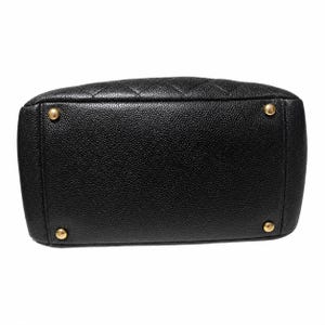 May include: Black leather handbag with a quilted top and gold-toned feet. The bottom of the bag is rectangular with rounded corners. The leather has a pebbled texture.