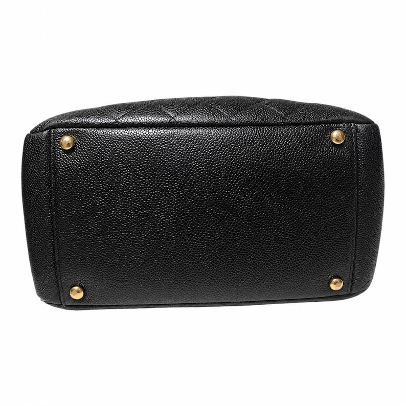 May include: Black leather handbag with a quilted top and gold-toned feet. The bottom of the bag is rectangular with rounded corners. The leather has a pebbled texture.