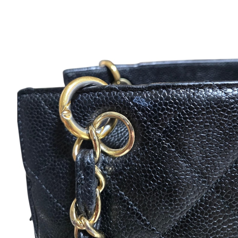 May include: Close-up of a black quilted leather handbag with gold-tone hardware. The bag features a chain strap and a textured surface. The gold hardware includes rings and a chain.