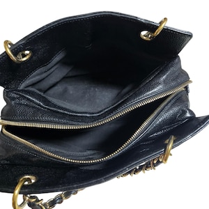 May include: Black leather handbag with gold-tone hardware. The bag features a top zipper closure and chain straps. The interior is lined with black fabric. The bag is open, revealing the interior compartments.