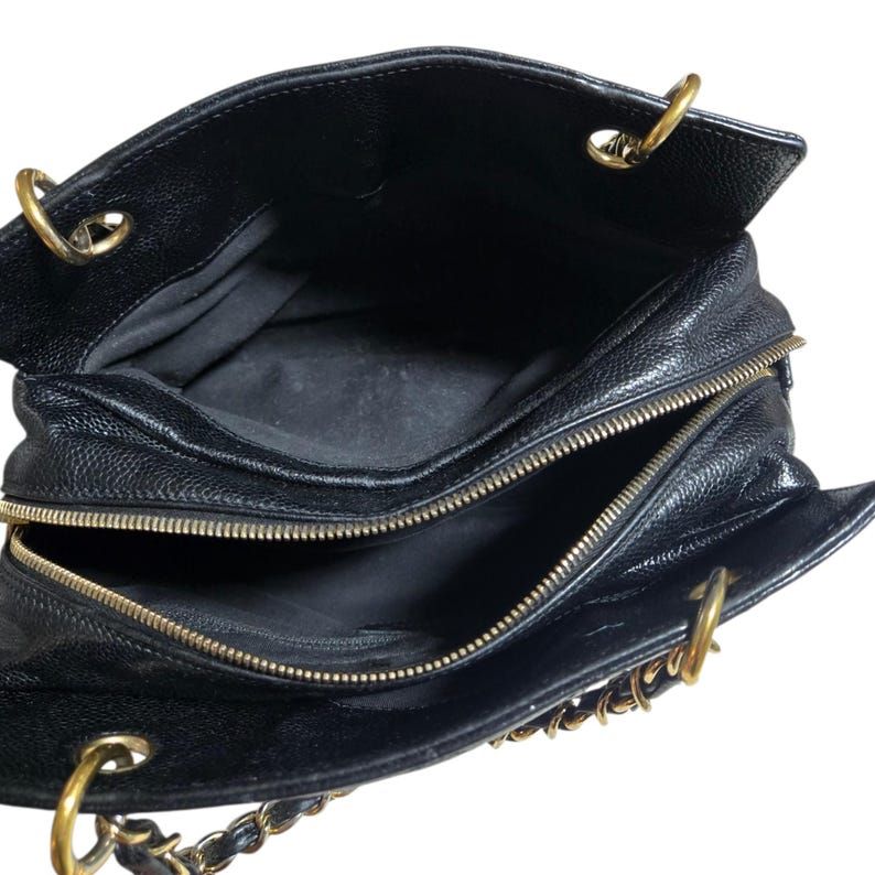 May include: Black leather handbag with gold-tone hardware. The bag features a top zipper closure and chain straps. The interior is lined with black fabric. The bag is open, revealing the interior compartments.