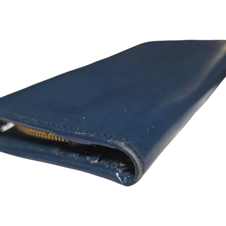 May include: A close-up of a navy blue wallet with a gold zipper. The wallet has a smooth, slightly glossy finish. The zipper is partially open, revealing the interior.