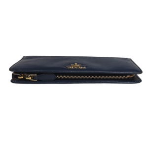 May include: A navy blue leather wallet with a gold-colored zipper and hardware. The wallet has a rectangular shape and a small gold-colored logo on the front. The zipper is closed.