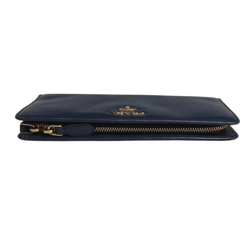 May include: A navy blue leather wallet with a gold-colored zipper and hardware. The wallet has a rectangular shape and a small gold-colored logo on the front. The zipper is closed.