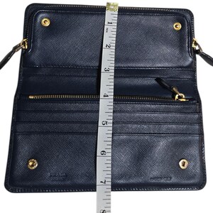 May include: Open navy blue wallet with gold-tone hardware, measuring approximately 7 inches in height. Features multiple card slots, a zippered compartment, and a snap closure. The brand name is visible. Made in Italy.