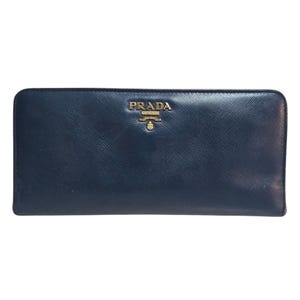 May include: A navy blue leather wallet with the gold-colored brand name "PRADA" embossed on the front. The wallet has a rectangular shape and a smooth texture. The Prada logo is centered above the wallet's midpoint.