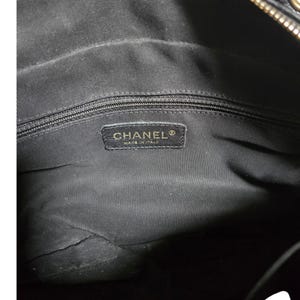 May include: Interior view of a black handbag. The lining is black fabric. A rectangular label with the brand name "CHANEL" and "MADE IN ITALY" is sewn into the lining. The zipper is visible at the top.