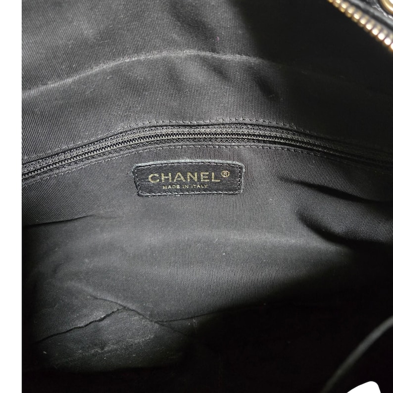 May include: Interior view of a black handbag. The lining is black fabric. A rectangular label with the brand name "CHANEL" and "MADE IN ITALY" is sewn into the lining. The zipper is visible at the top.