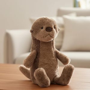 Op de afbeelding: Een bruin otter knuffel met een zacht, getextureerd uiterlijk. Het knuffeldier heeft een ronde kop, kleine oren en een donkerbruine neus. Het zit rechtop met uitgestrekte armen en benen.