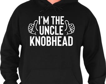 Pode incluir: Moletom preto com a frase branca "I'M THE UNCLE KNOBHEAD", ladeada por ilustrações de polegares para cima. A peça inclui um bolso frontal e um capuz com cordão.