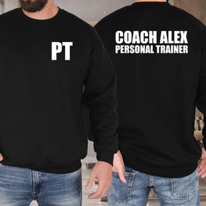Könnte beinhalten: Schwarzes Sweatshirt mit Rundhalsausschnitt und weißem Text. Auf der Vorderseite des Sweatshirts steht "PT" in großen, fetten Buchstaben. Auf der Rückseite des Sweatshirts steht der Text "COACH ALEX PERSONAL TRAINER" in gestapelter Form. Das Sweatshirt wird von einer Person getragen.