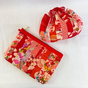 May include: Two red fabric pouches with floral patterns. One is a rectangular zippered pouch, and the other is a round drawstring bag. Both are made of patchwork fabric with various floral and geometric designs in shades of red, pink, and white.