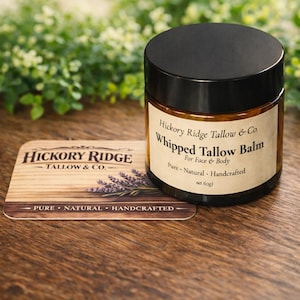 May include: A jar of Hickory Ridge Tallow & Co. Whipped Tallow Balm for Face & Body, with a black lid and a label. A wooden coaster with the company logo and lavender sprigs is next to the jar. The text on the label reads "Pure - Natural - Handcrafted" and "net 60g".