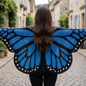 May include: A crochet shawl designed to resemble butterfly wings, featuring a vibrant blue and black pattern with small white accents along the edges. The garment is worn over the shoulders, extending outward to mimic the shape of wings.