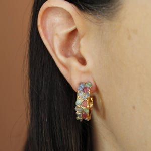 May include: Gold hoop earrings with a cluster of colourful gemstones. The earrings feature blue, pink, and green stones set in gold metal. A unique and eye-catching accessory, perfect for adding a touch of colour.